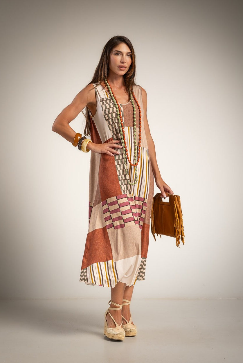 A woman models a sleeveless, round neck maxi dress with a patchwork print in beige, brown, and orange tones