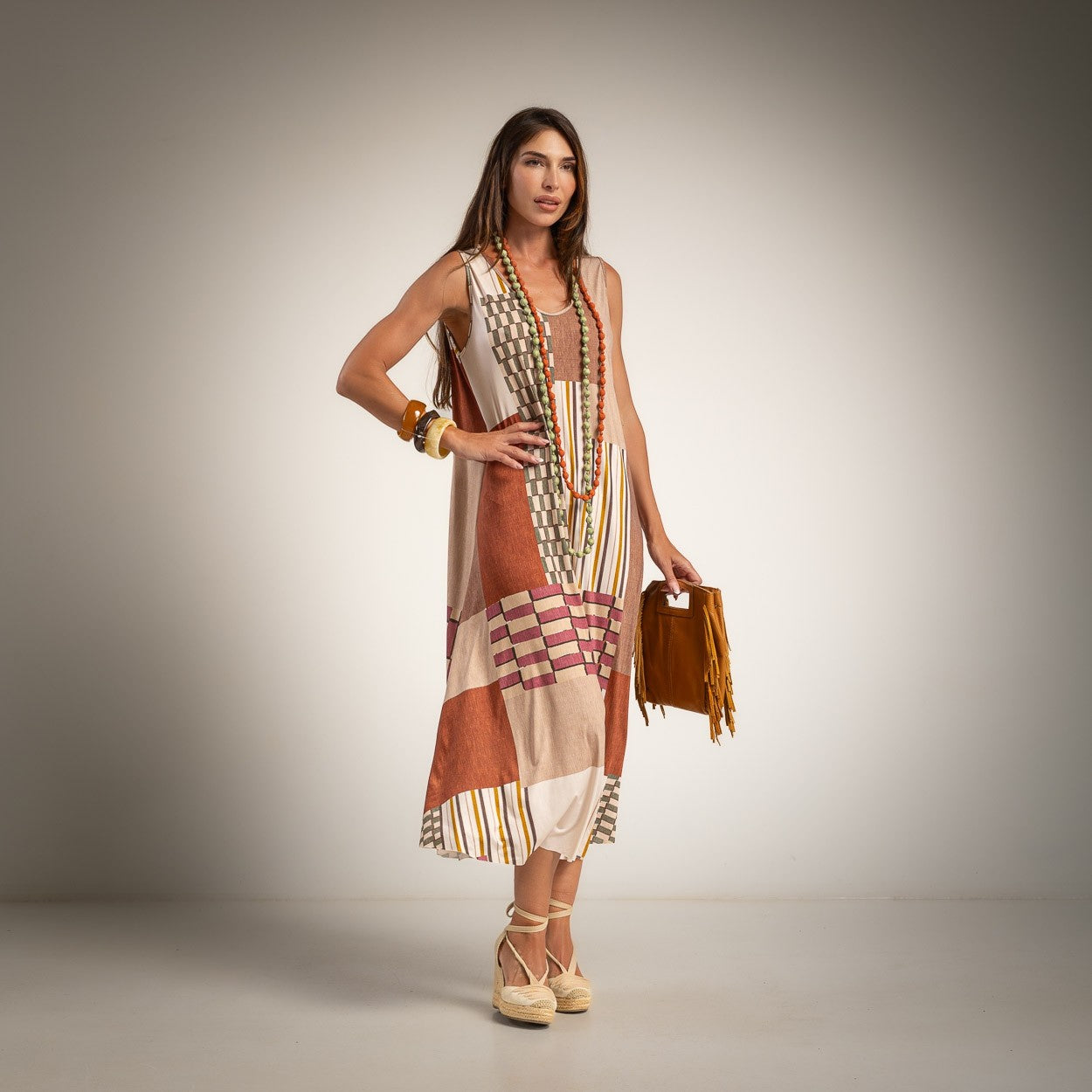 A woman models a sleeveless, round neck maxi dress with a patchwork print in beige, brown, and orange tones