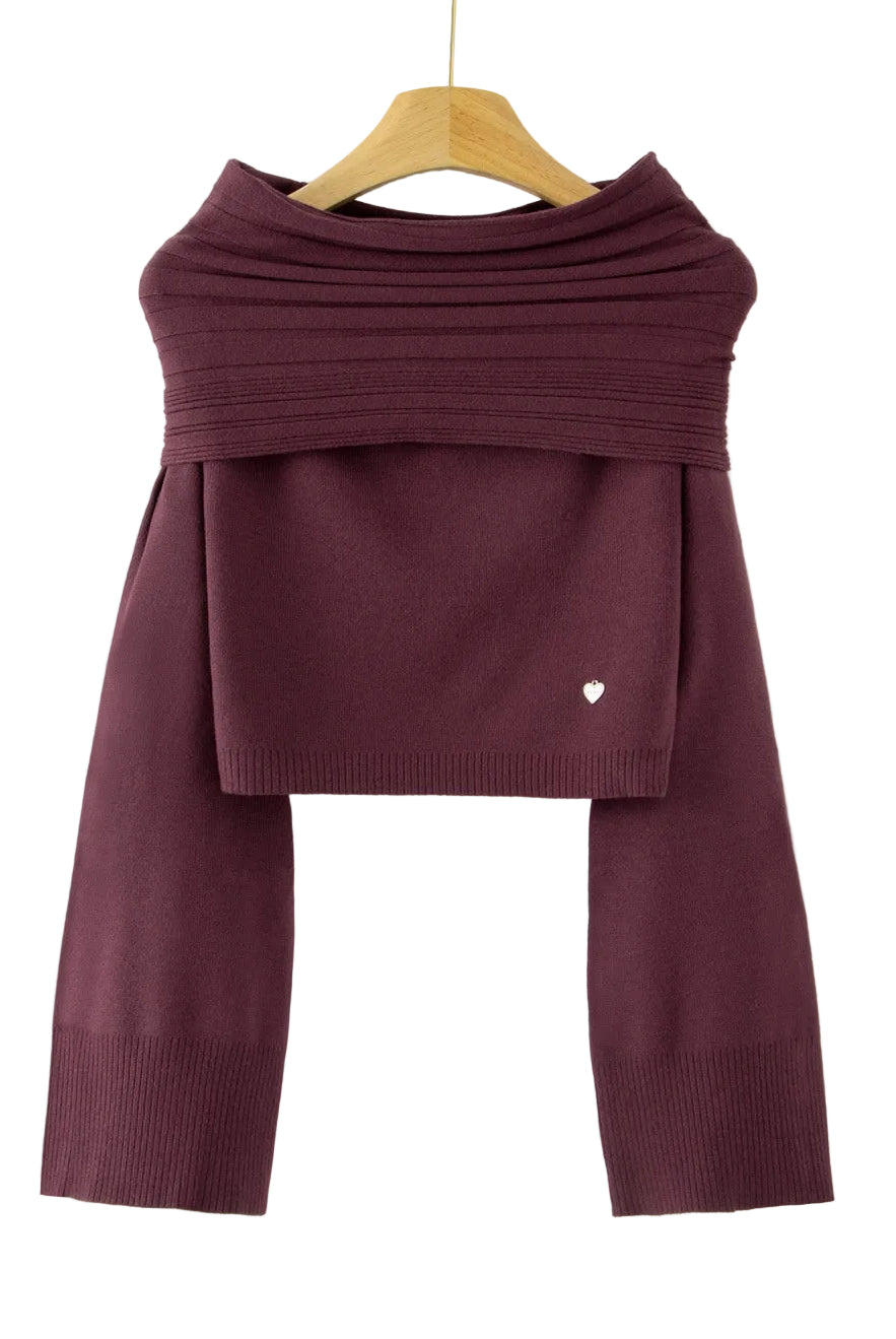 A dark plum purple knit long-sleeve top with a draped, layered cowl neck design, hanging on a wooden hanger against a plain white background. A small white heart detail is visible on the lower right of the front panel.