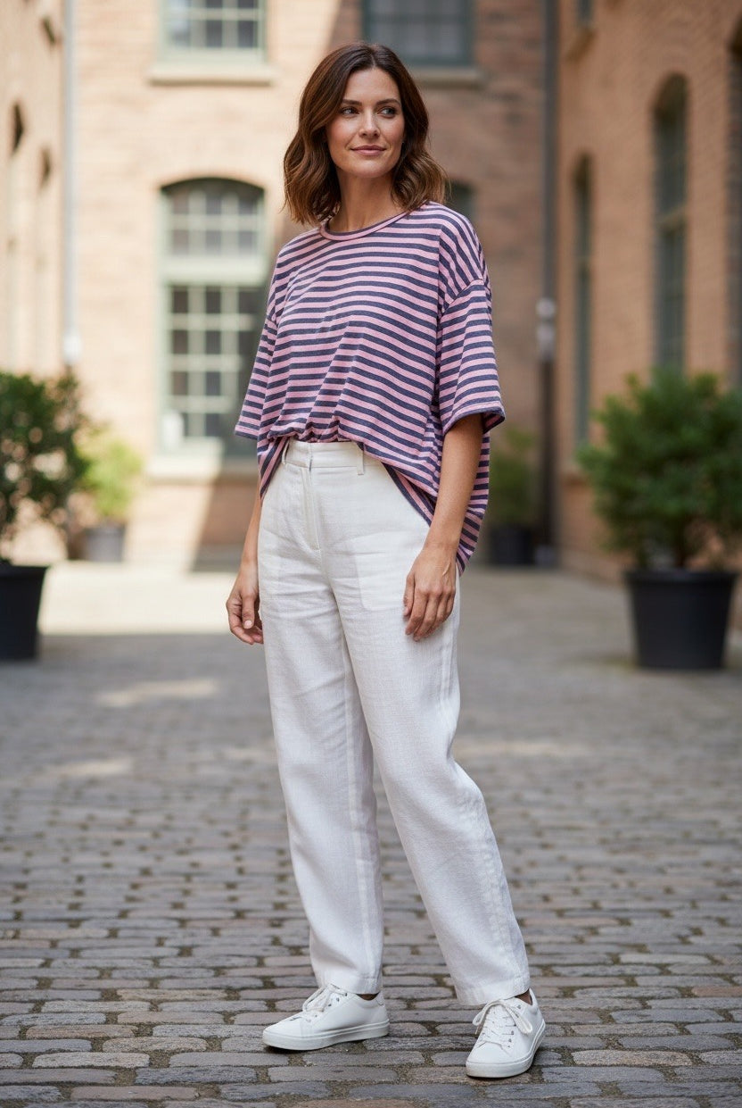 Woman wearing a striped shirt and white pants standing on a cobblestone street.