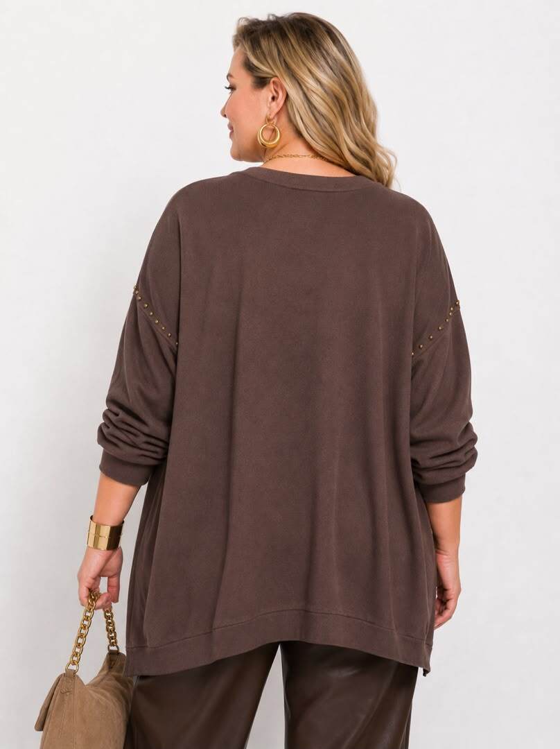 A woman shown from the back wearing an oversized brown long-sleeve top with decorative gold chain details along the upper sleeves, paired with brown pants, against a plain light background.