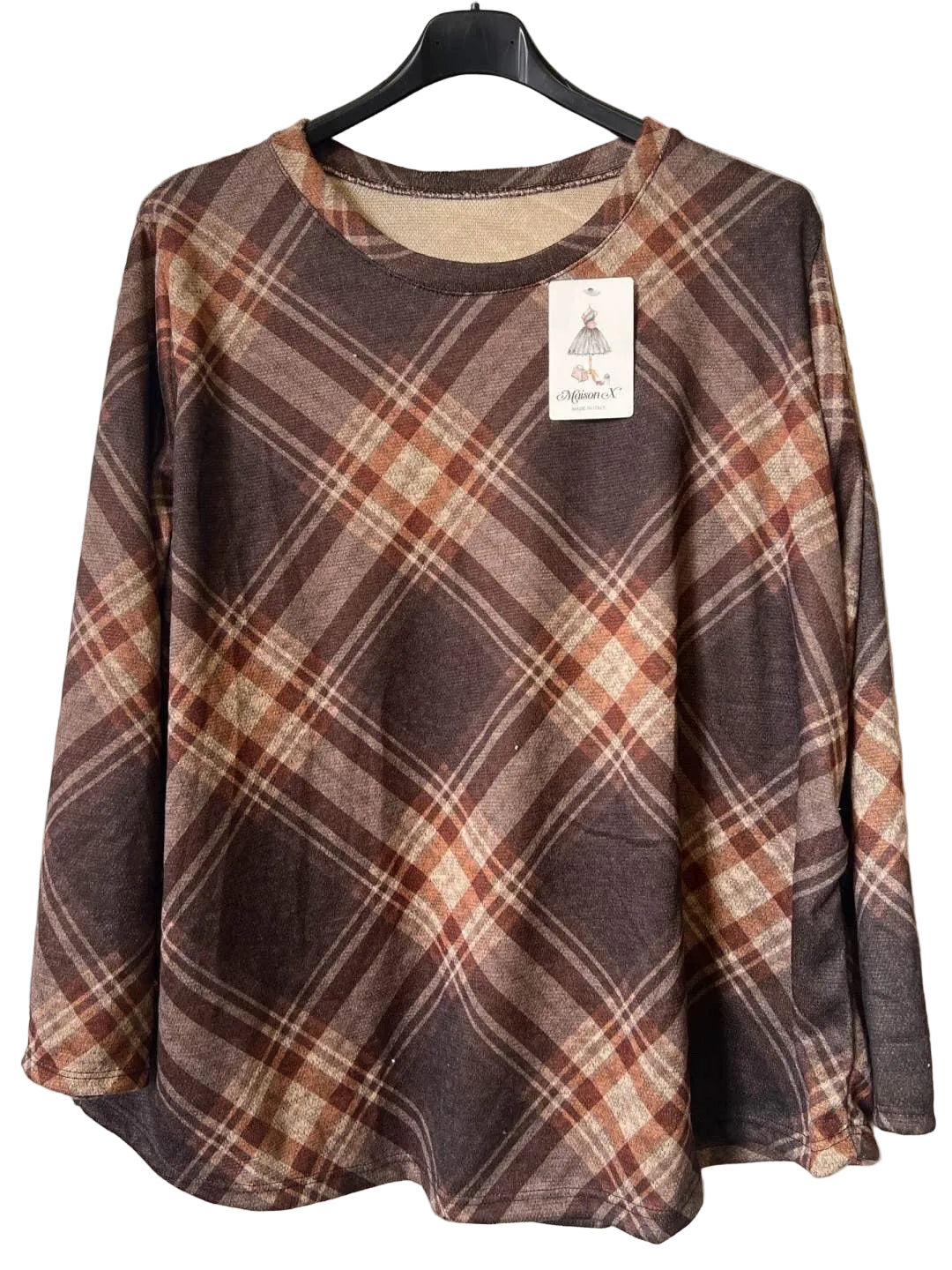 A long-sleeve plaid top hanging on a black hanger against a textured gray wall. The top features a brown, rust-orange, and beige plaid pattern