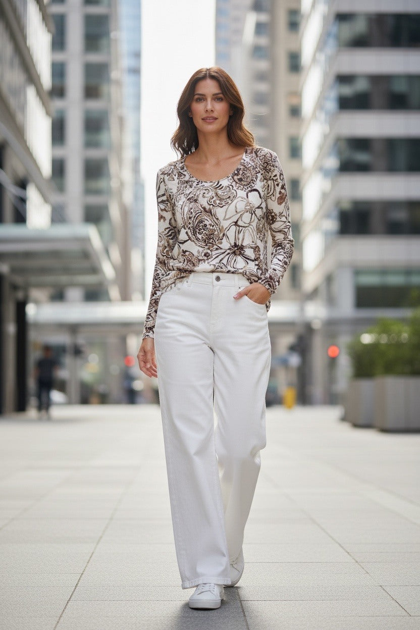 A woman walking down a city street wearing a beige and brown floral long-sleeve top with white wide-leg trousers and white sneakers.