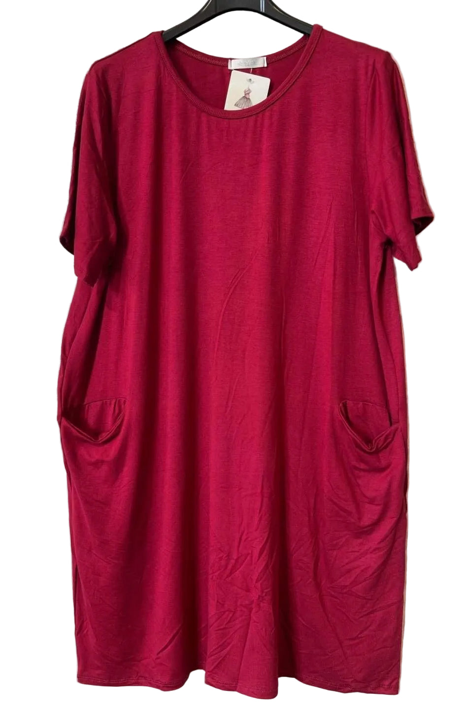 A short-sleeve crewneck dress in a burgundy colour, hanging on a black hanger against a textured gray wall. The dress features side pockets and a small white brand tag at the neckline.