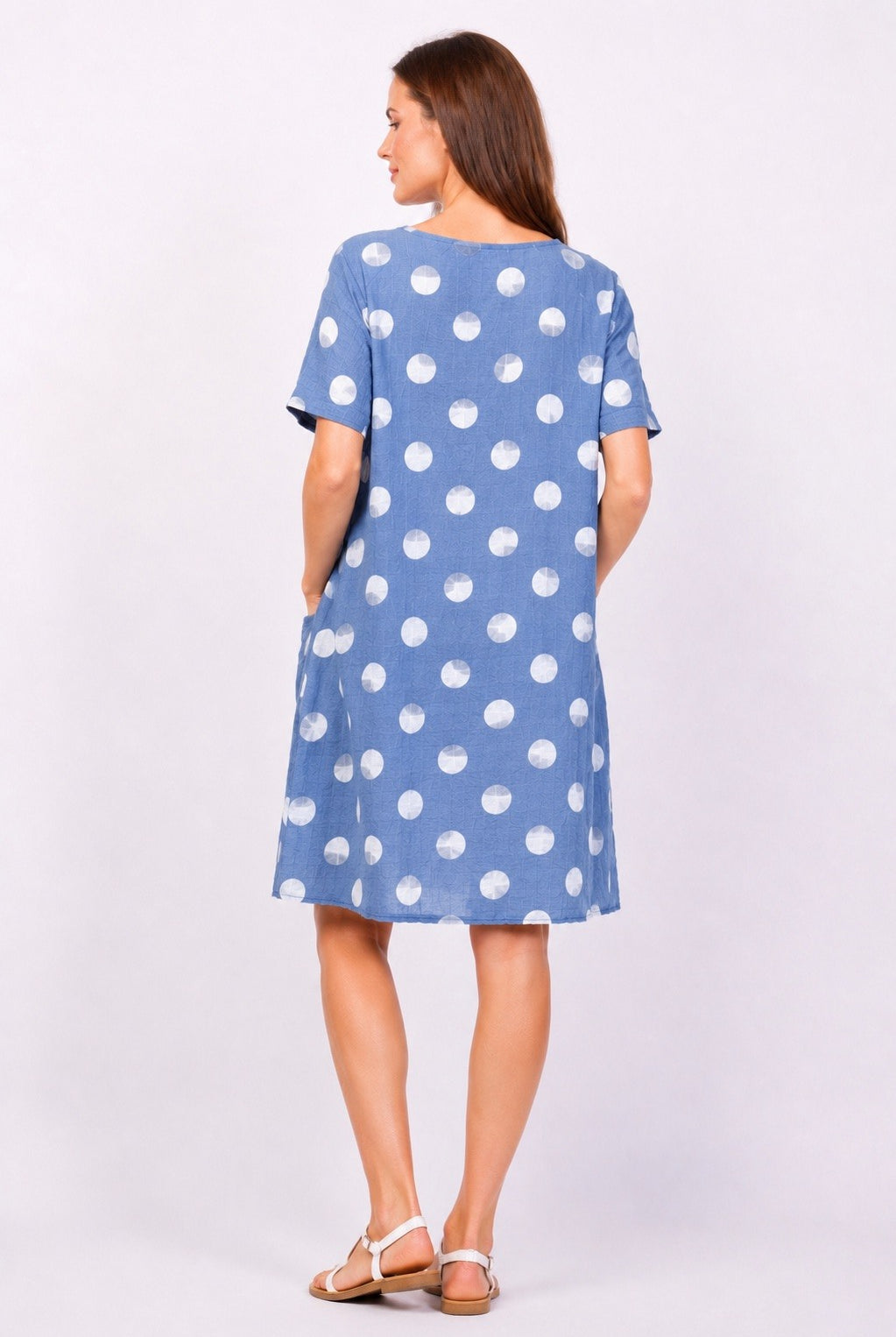 Woman wearing a blue dress with white polka dots on a plain background