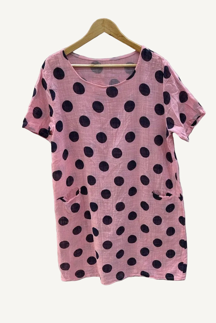 Pink dress with black polka dots on a hanger against a white background