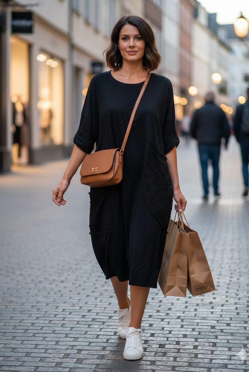 Woman in a black dress with a brown handbag walking on a street.