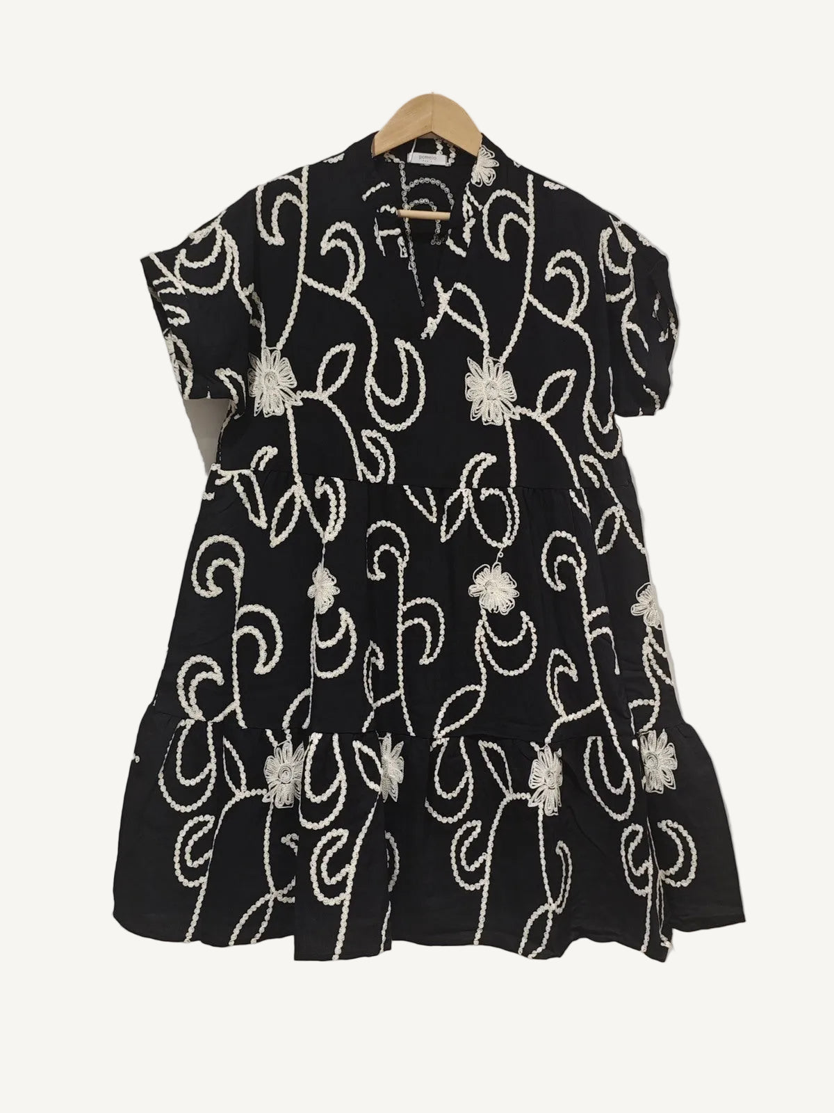 Black dress with white floral patterns on a hanger against a white background