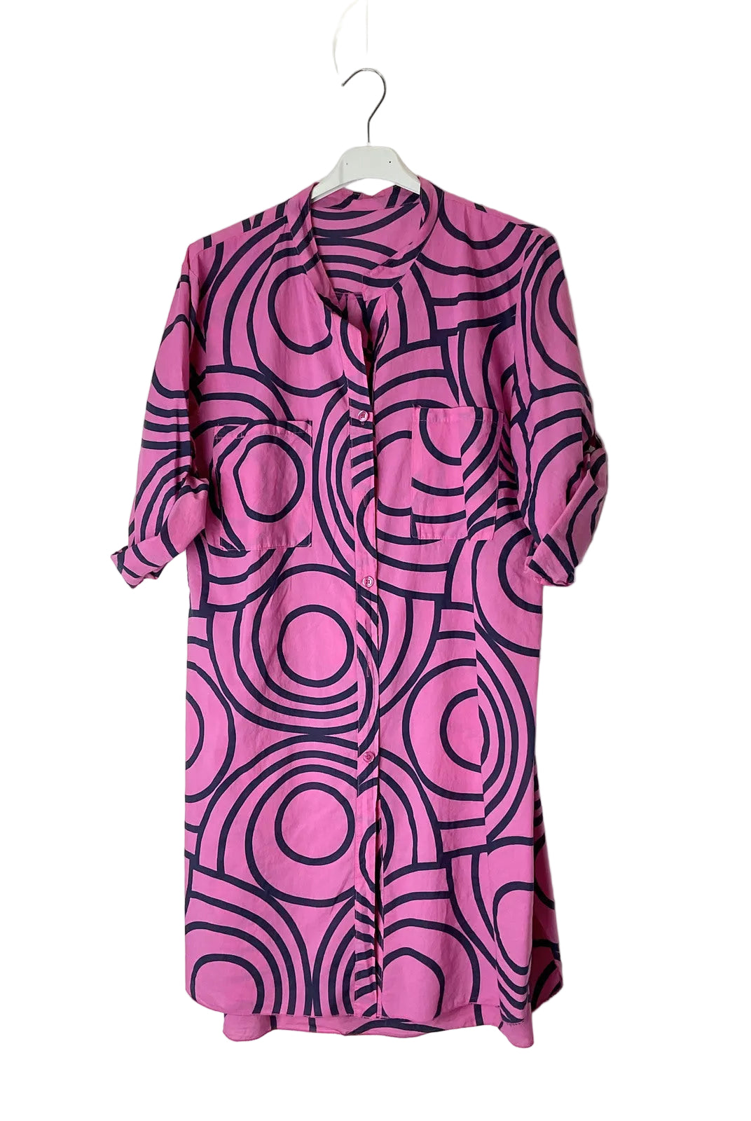A pink and black geometric patterned shirt dress hanging on a white plastic hanger against a plain white wall.
