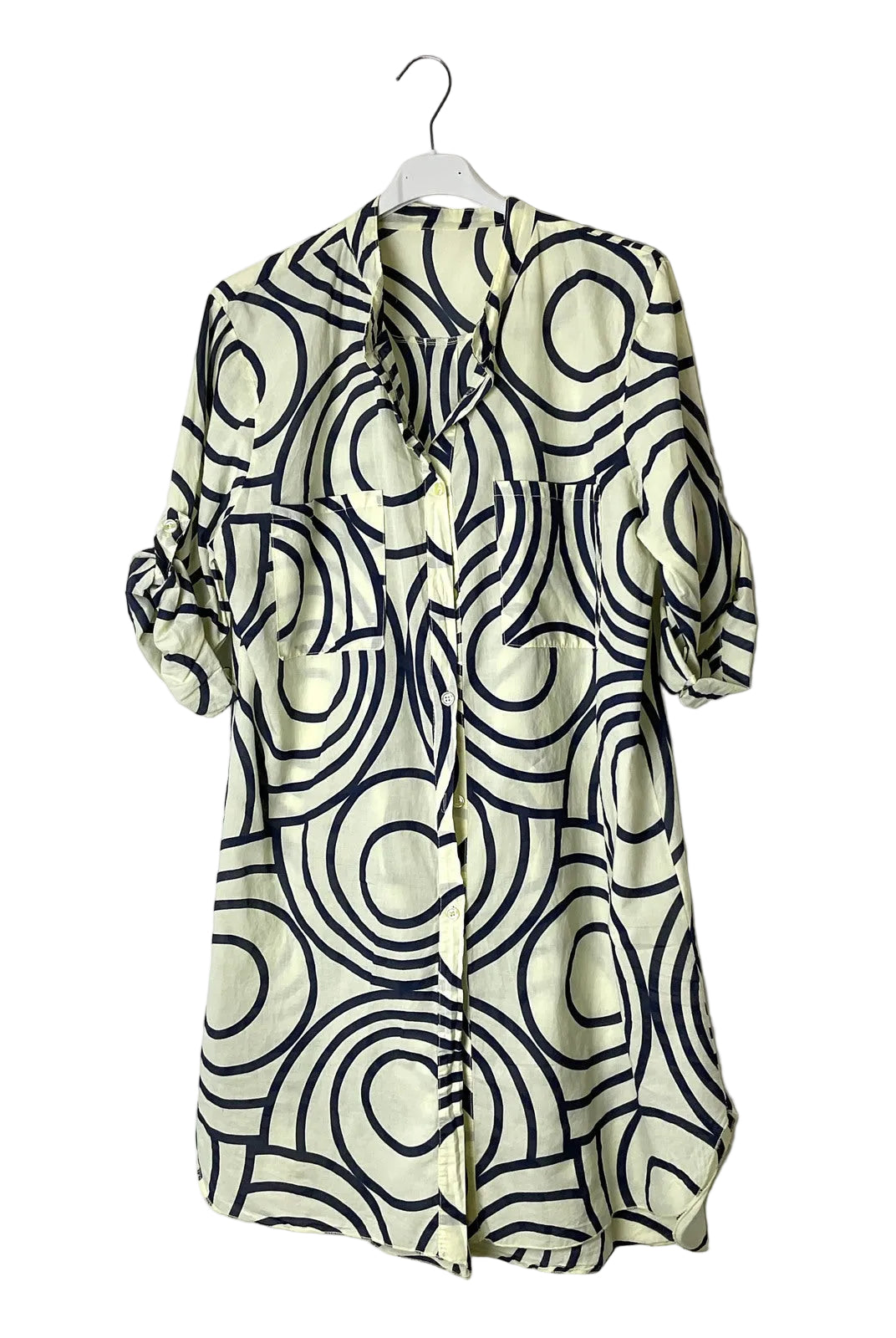 A short-sleeve button-front shirt dress with a cream base and a bold black wavy geometric pattern, hanging on a white plastic hanger against a plain white wall.