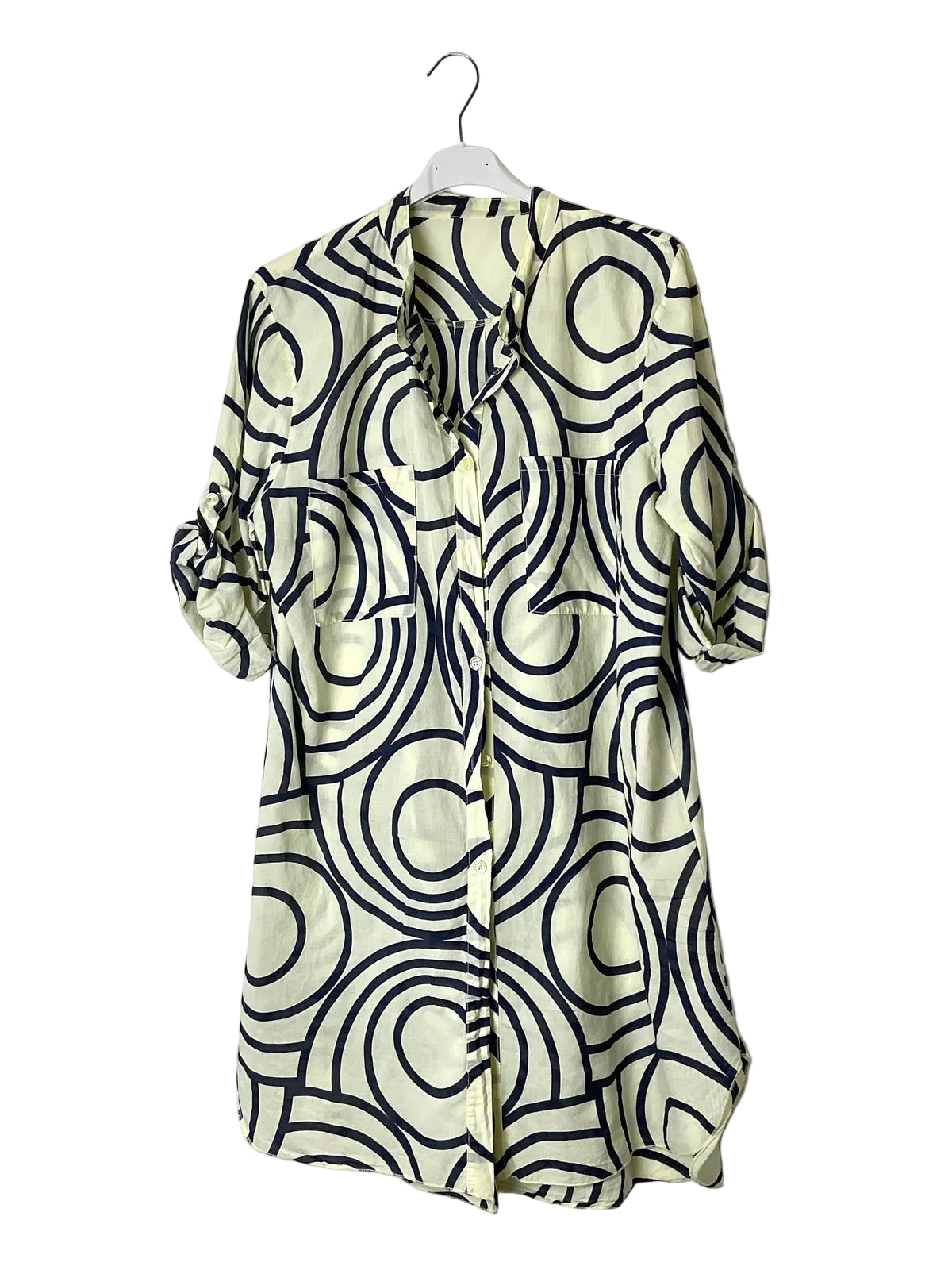 A short-sleeve button-front shirt dress with a cream base and a bold black wavy geometric pattern, hanging on a white plastic hanger against a plain white wall.