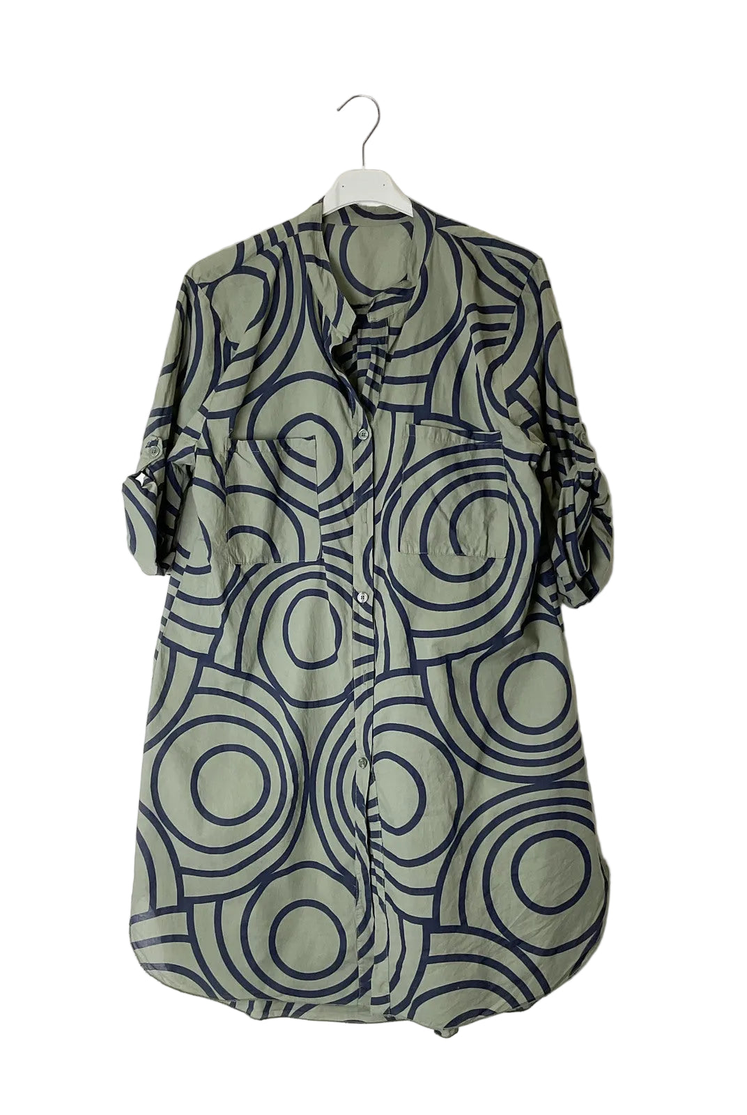An olive green button-up shirt dress with abstract circular pattern, hanging on a white plastic hanger against a plain white wall.