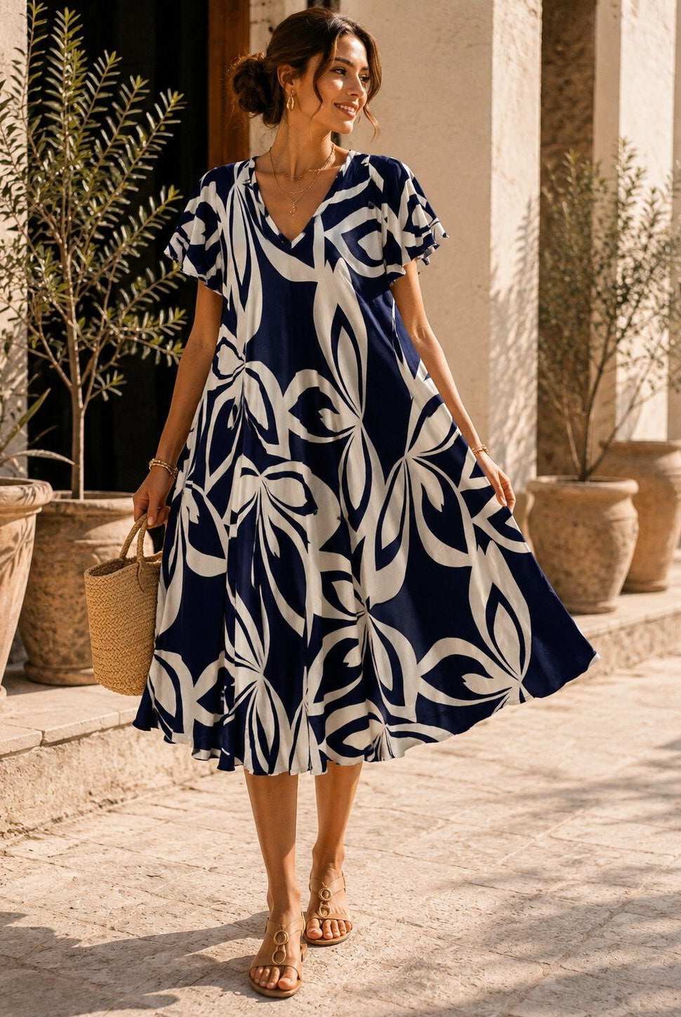Woman wearing a blue and white patterned dress standing outdoors with plants and columns in the background.