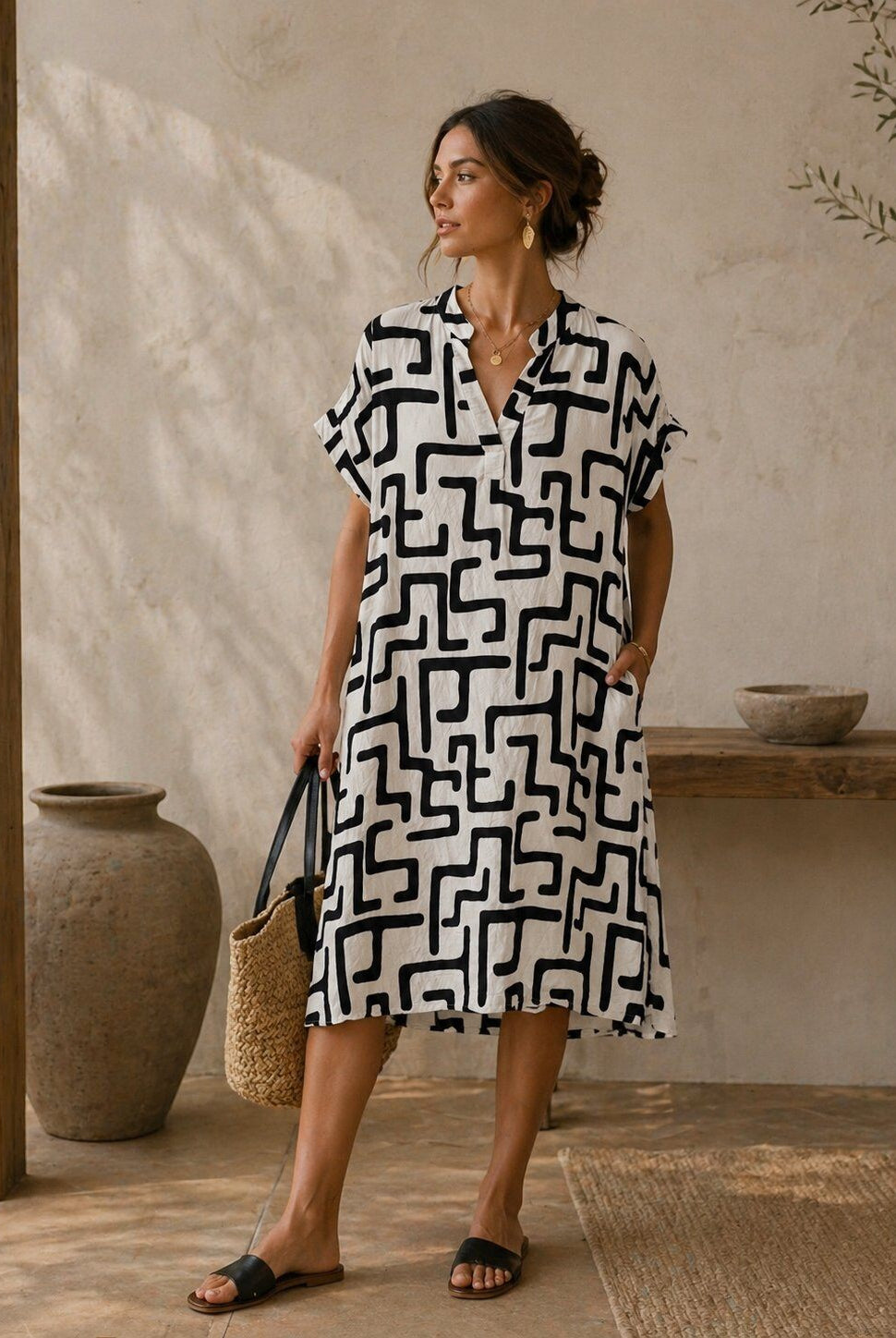 Woman wearing a black and white patterned dress standing in a rustic indoor setting.