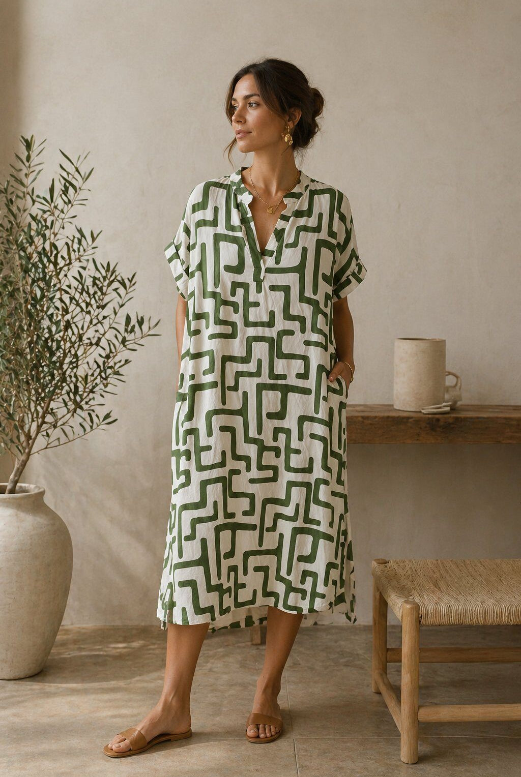 Woman wearing a green and white patterned dress standing in a room with a plant and wooden stool.