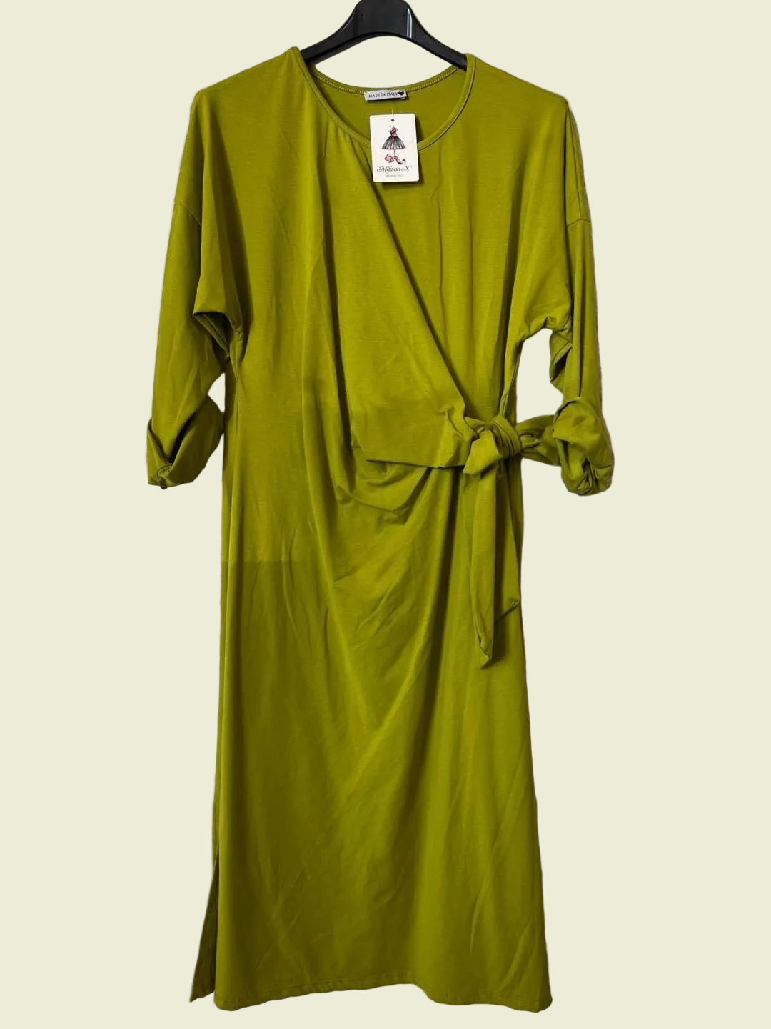 An olive green wrap-style midi dress with three-quarter sleeves and a self-tie waist belt, hanging on a black hanger against a textured gray wall.