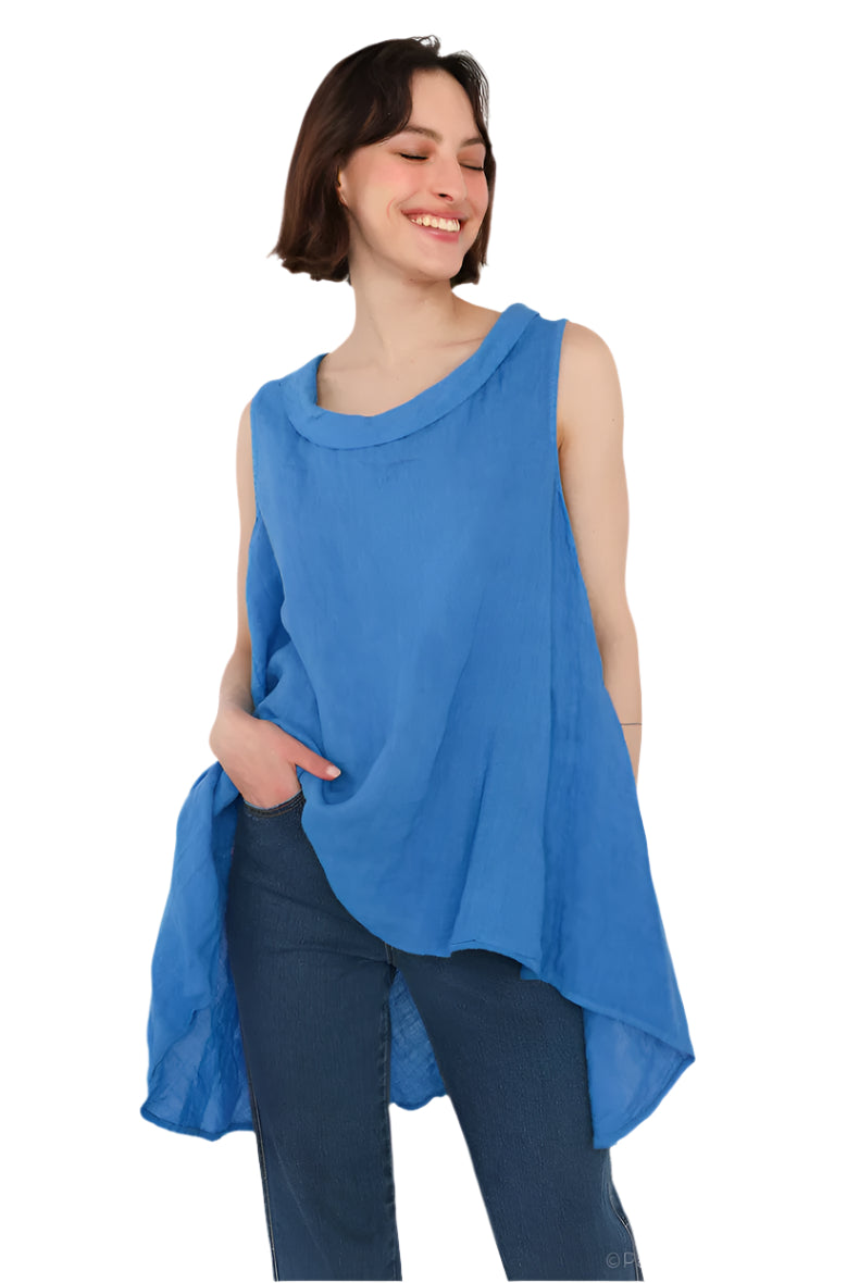 A woman wearing a royal blue sleeveless cowl neck top with an asymmetrical hem, paired with white trousers.