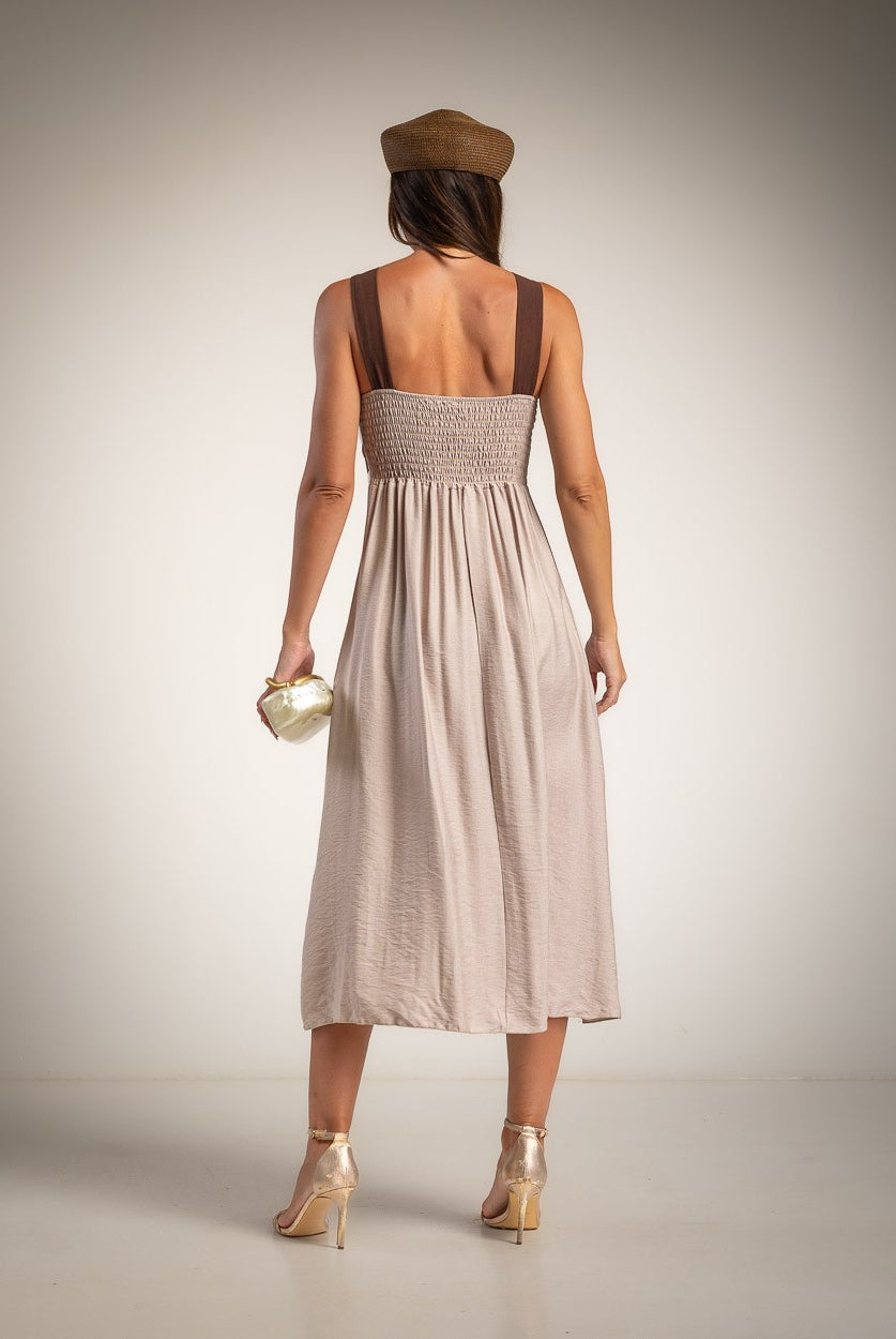 A woman is shown from behind wearing a light taupe midi dress with brown shoulder straps and a shirred back