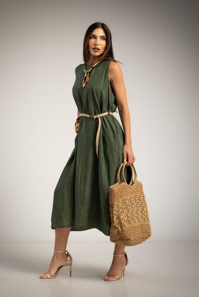 A woman models a sleeveless khaki green midi dress with a beige tie belt, holding a woven straw tote bag