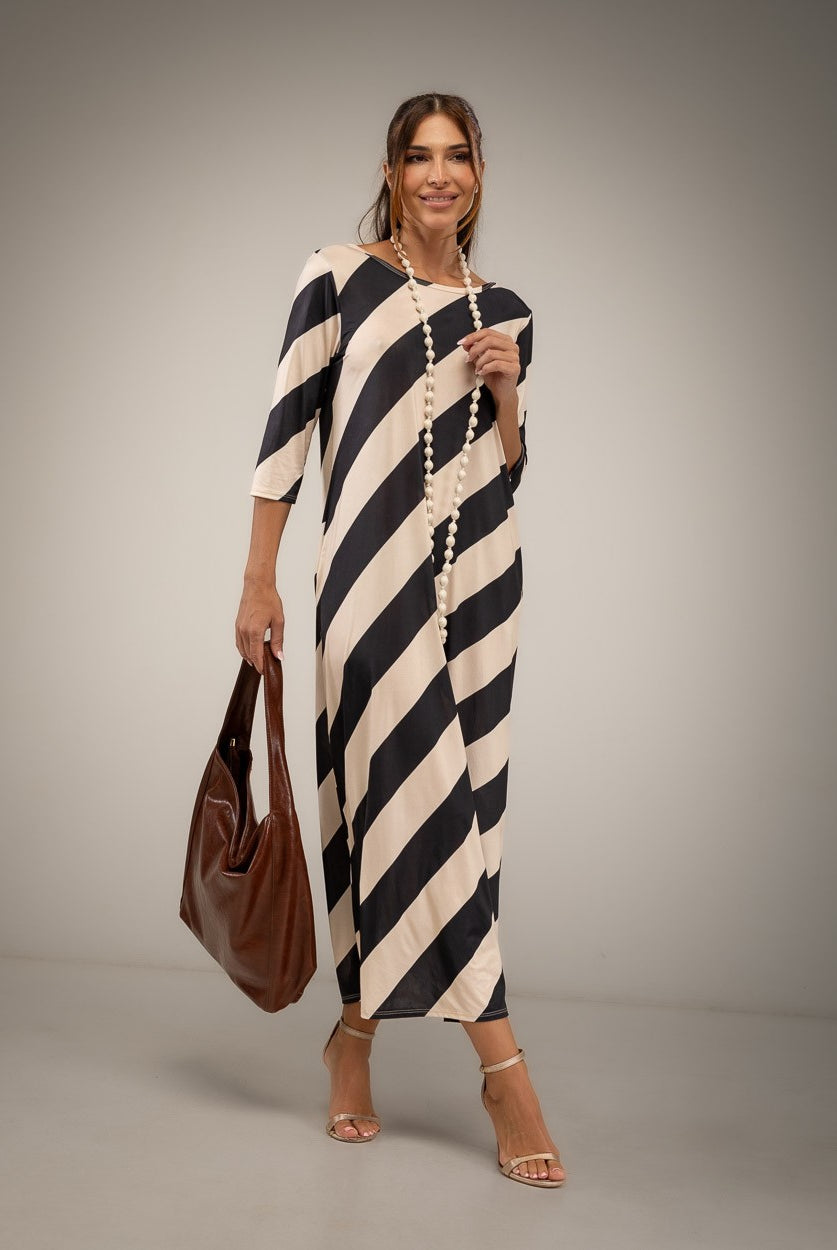 A woman modeling a black and cream diagonal striped midi dress with elbow-length sleeves, holding a brown leather tote bag