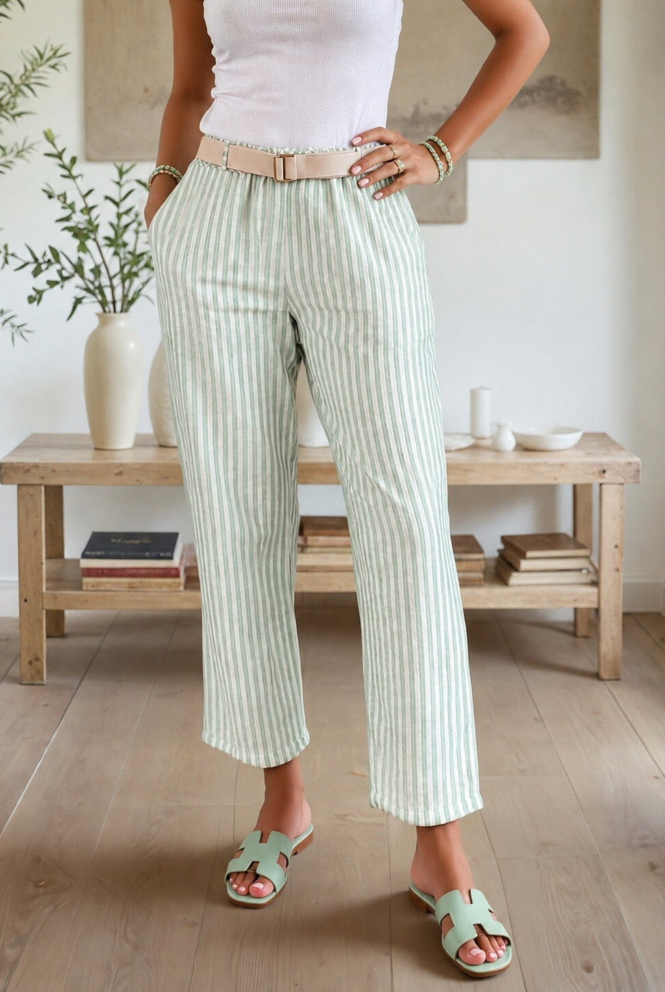 Person wearing light green striped pants and white top in a room with wooden furniture and plants.