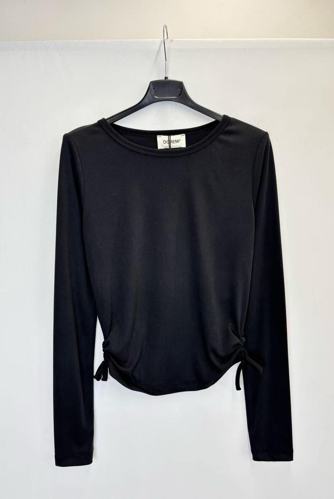 A black long-sleeve crop top with side tie details, hanging on a black hanger against a plain white wall.