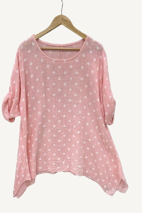 Pink polka dot shirt on a hanger against a light gray background