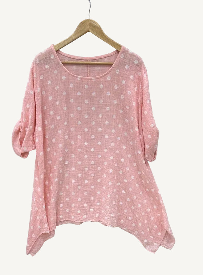 Pink polka dot shirt on a hanger against a light gray background