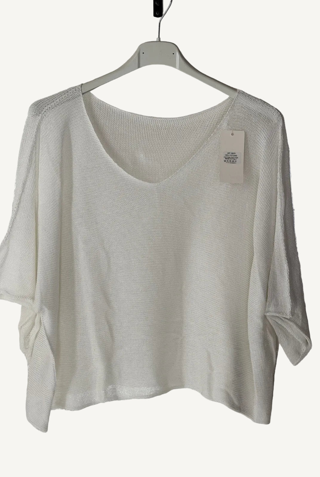 White sweater on a hanger with a visible tag against a textured white background