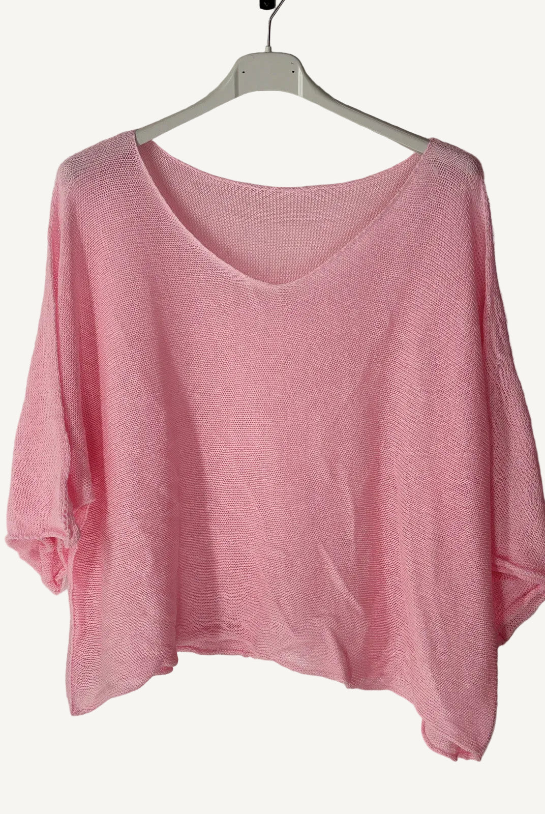 Pink sweater on a hanger against a textured wall.