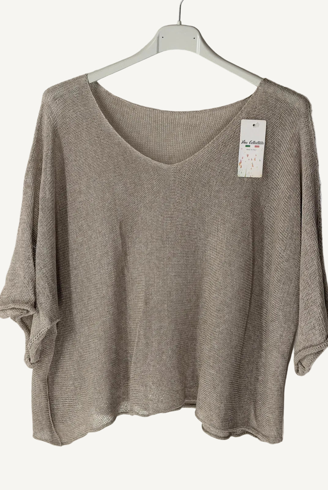 Brown sweater on a hanger with a tag against a textured wall.