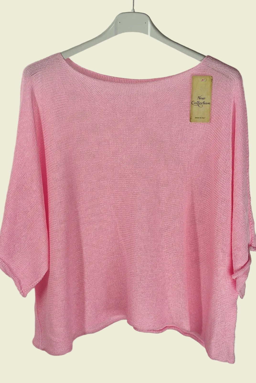 Pink sweater on a hanger with a visible tag against a neutral background