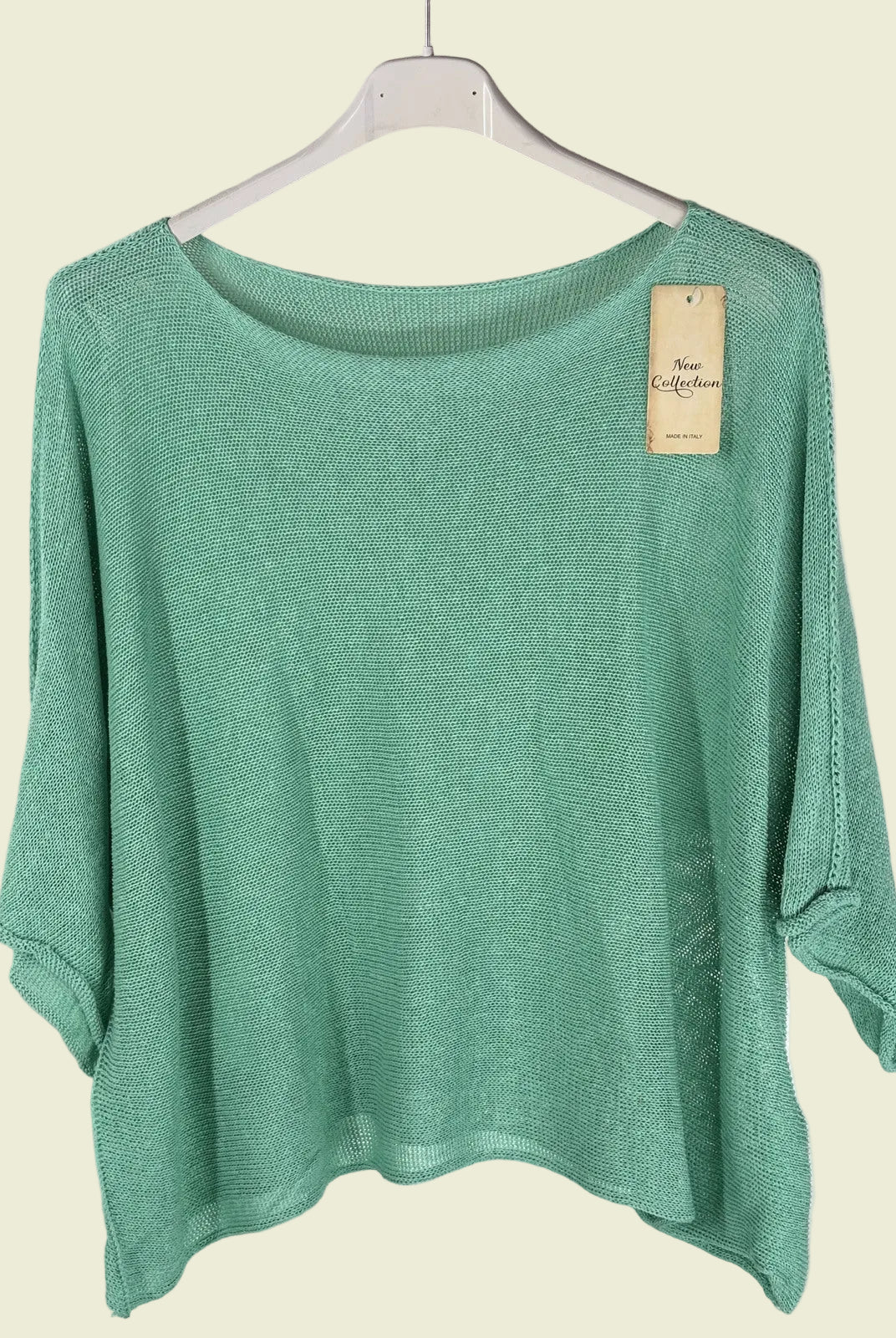 Green sweater on a hanger with a visible tag against a textured wall.