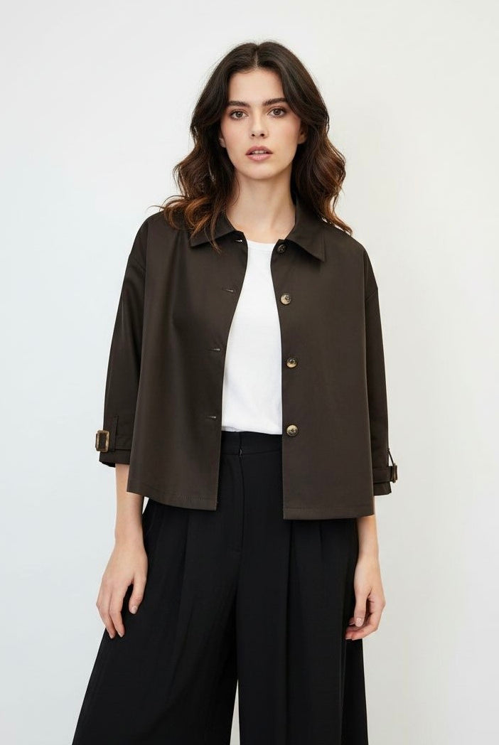 A woman modeling a dark brown cropped button-up jacket with three-quarter sleeves, worn over a white top and wide-leg trousers
