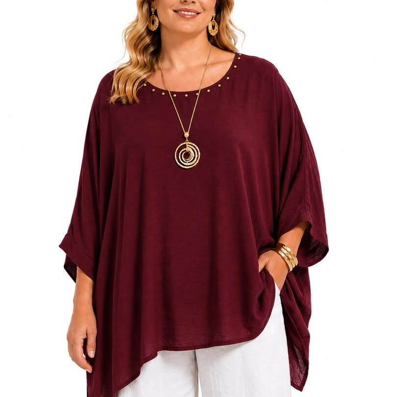 A woman modeling a loose-fitting, scoop-neck top in deep burgundy with small gold stud embellishments around the neckline, paired with white pants and gold jewelry, against a plain white background.