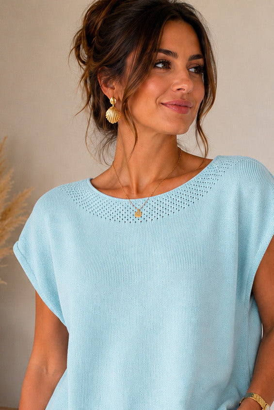 Woman wearing a light blue top and white pants, with product details displayed.