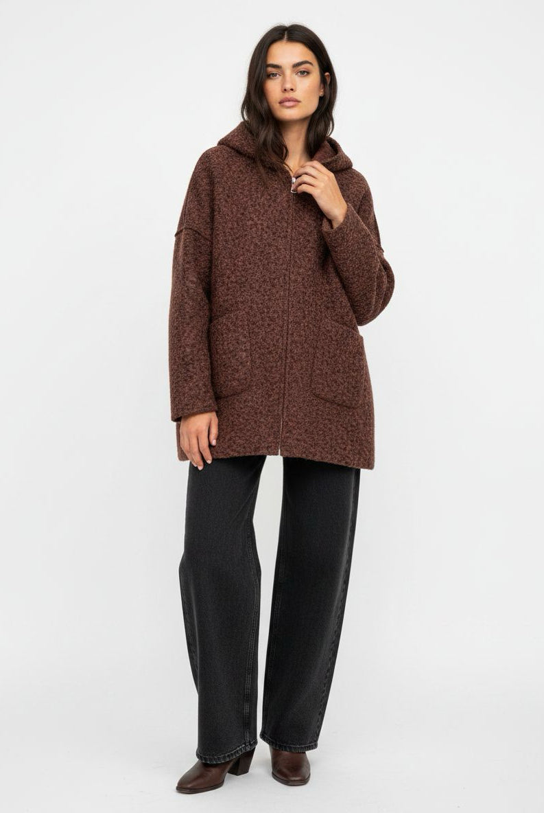 A woman modeling a brown textured hooded jacket with black wide-leg jeans and brown boots