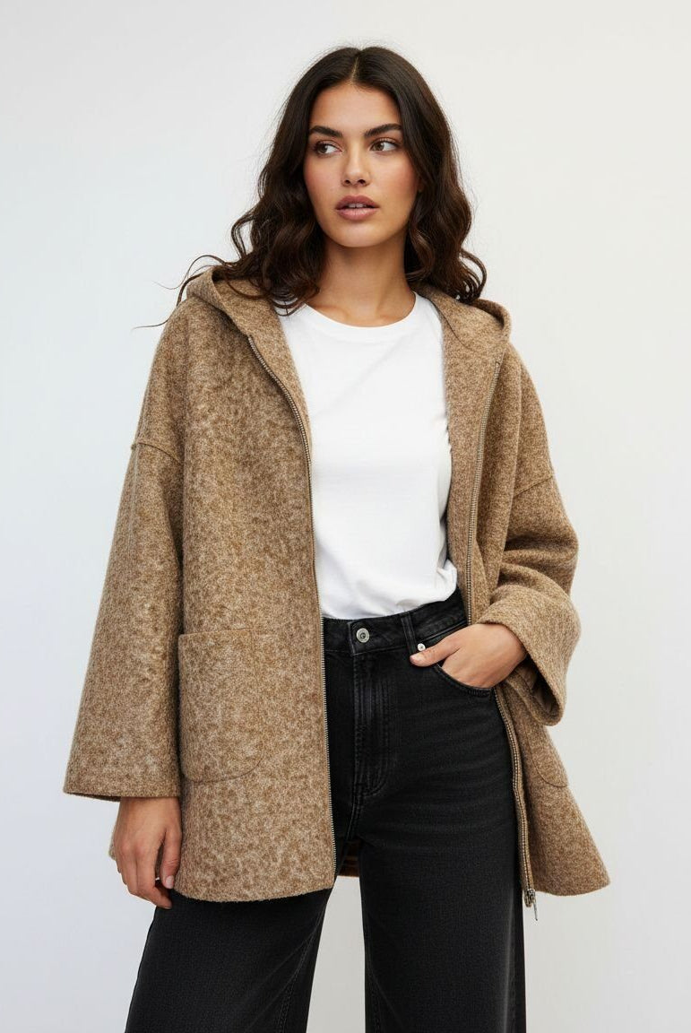 A woman modeling a textured, oversized camel-colored hooded coat over a white t-shirt and black jeans