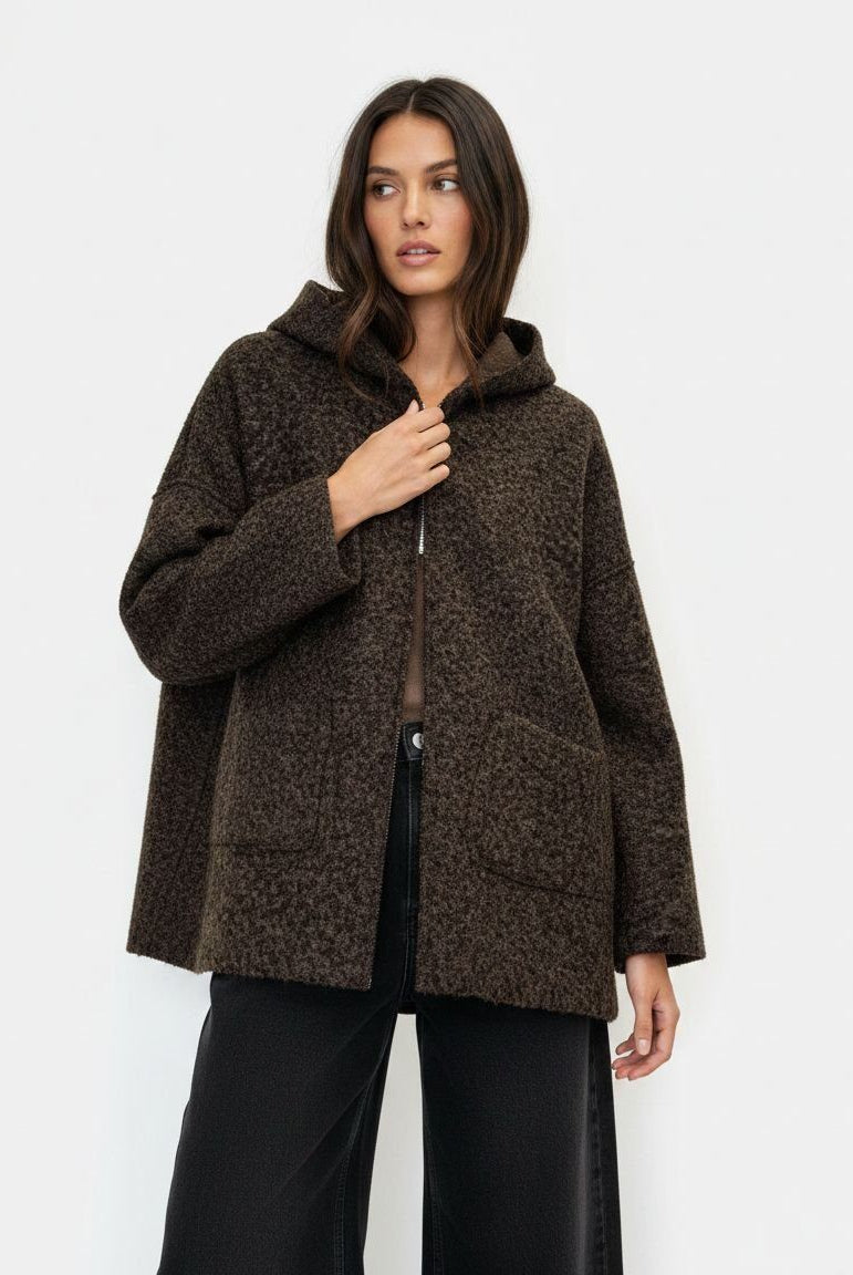 A woman modeling a dark brown textured hooded jacket with a fuzzy boucle-like pattern, paired with black wide-leg pants