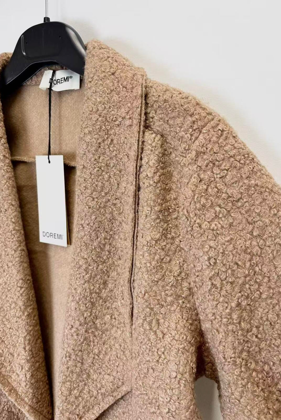 A close-up of textured bouclé coat in a warm camel beige color, hanging on a black hanger