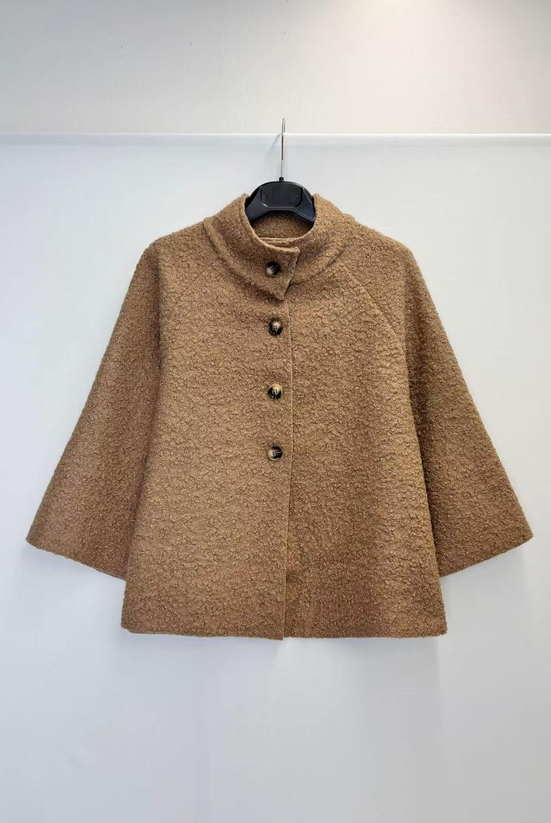 A brown textured bouclé jacket with a mock neck and three-quarter sleeves, hanging on a black hanger against a plain white wall.
