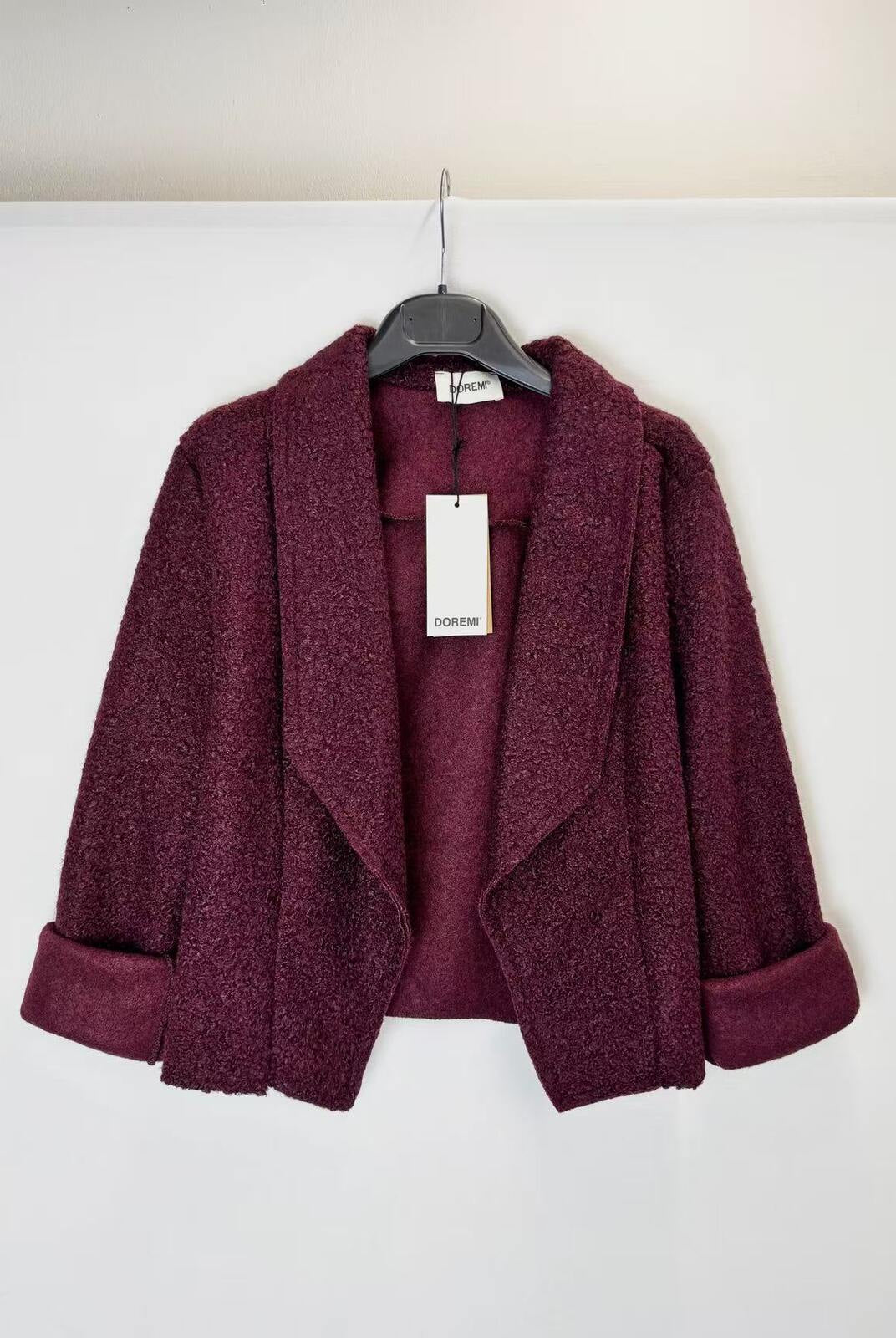 A textured, open-front cropped jacket in a deep plum purple color, hanging on a black hanger