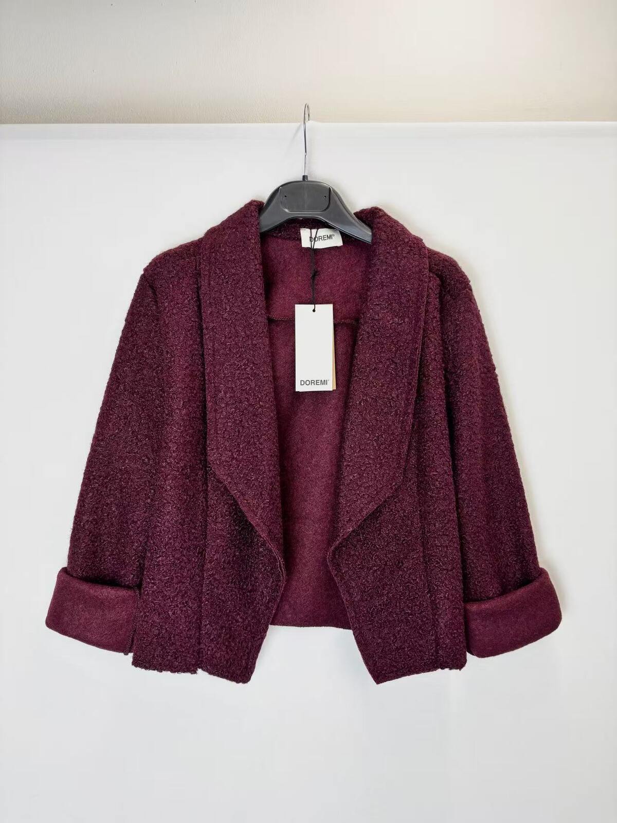 A textured, open-front cropped jacket in a deep plum purple color, hanging on a black hanger