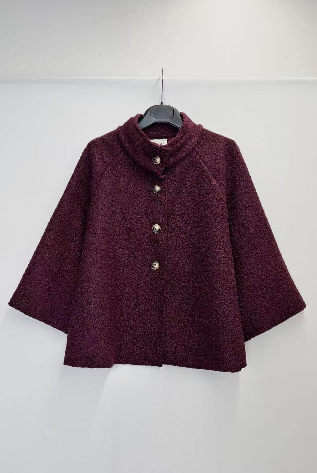 A dark burgundy textured jacket with a mock neck and three silver buttons, hanging on a black hanger against a plain white wall.