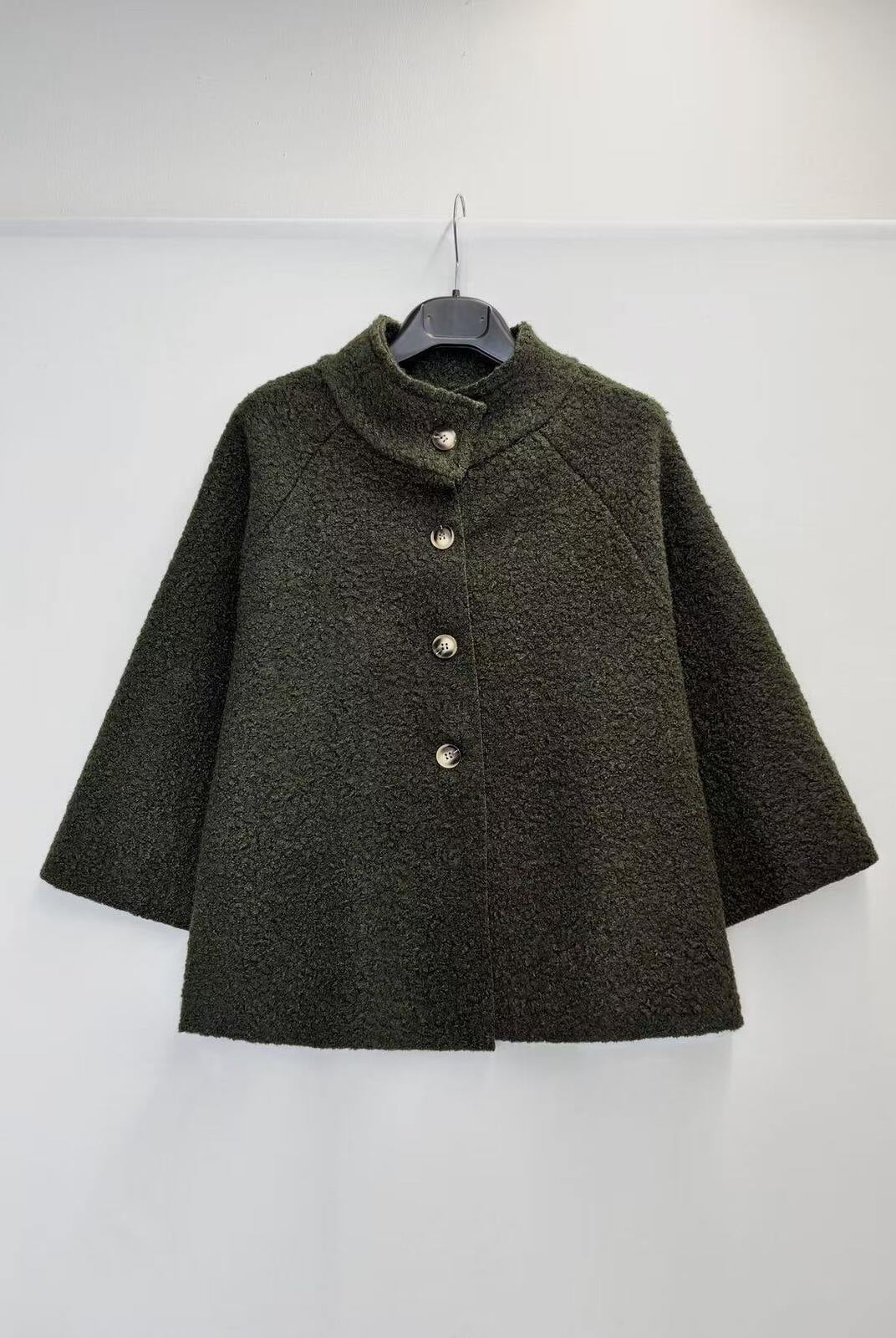 A dark olive green textured jacket with a mock neck and three front buttons, hanging on a black hanger against a plain white wall.