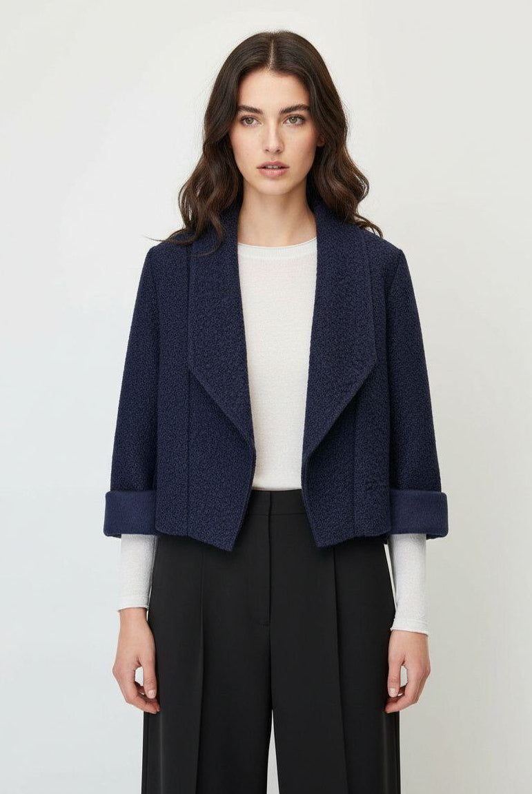 A woman modeling a cropped navy blue textured jacket with wide lapels and rolled cuffs, worn over a white top and black trousers