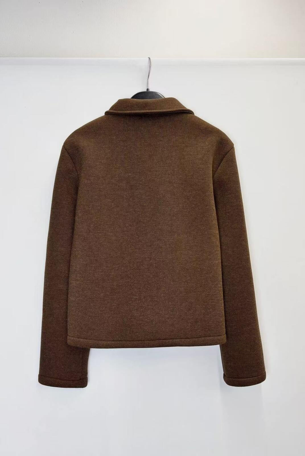 A brown long-sleeve knit top or sweater shown from the back, hanging on a black hanger against a plain white wall.