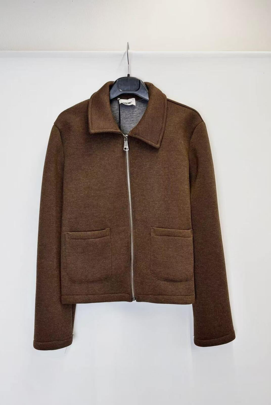 A brown zip-up jacket with a collar and two front patch pockets, hanging on a black hanger against a plain white wall.