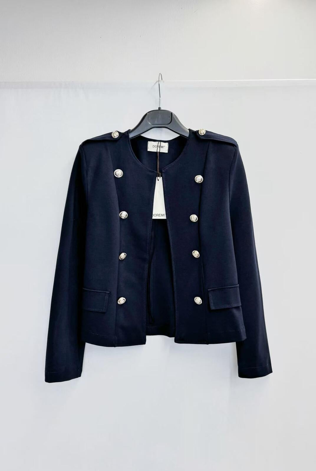 A dark navy blue cropped military-style jacket with silver-tone buttons, hanging on a black hanger against a plain white wall.