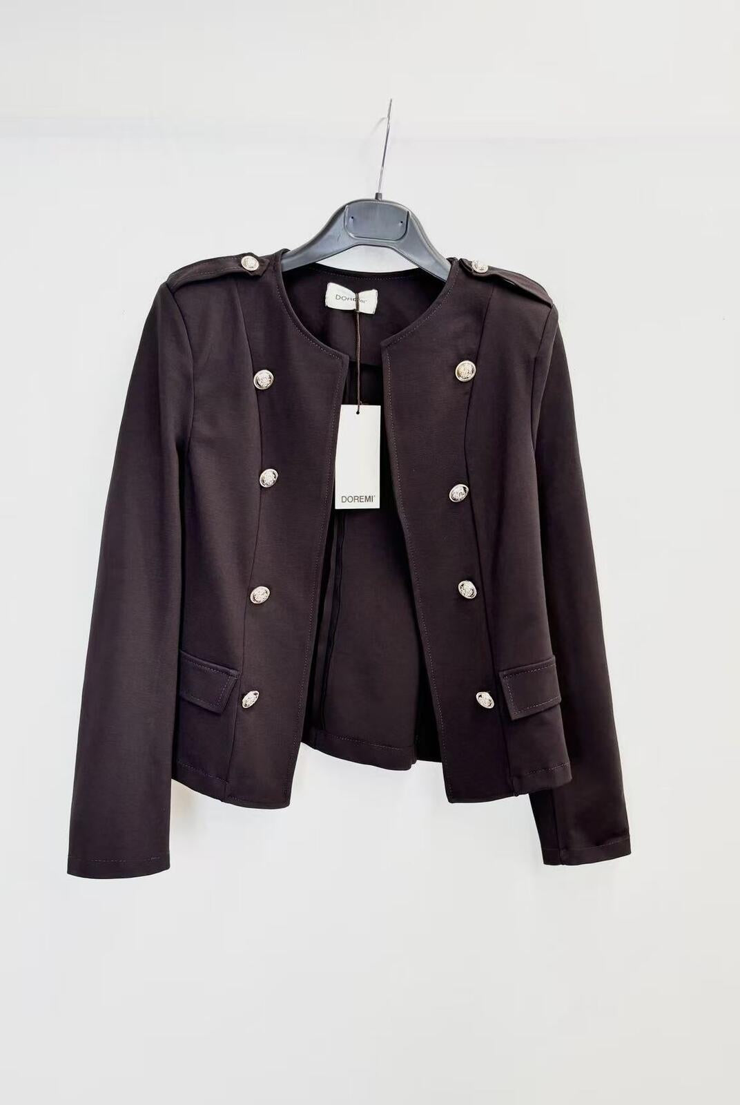 A dark brown cropped military-style jacket with silver buttons, hanging on a black hanger against a plain white wall.